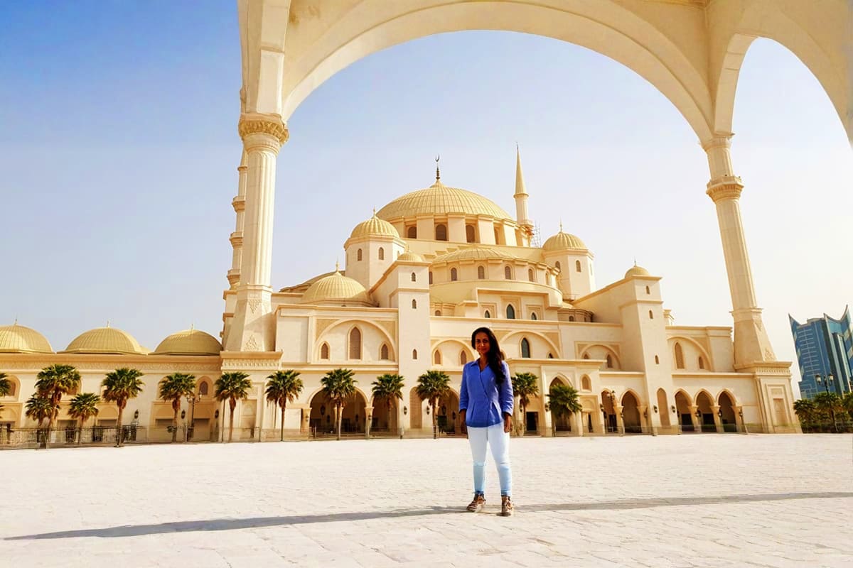 Woman standing in courtyard of Al-Hajar Mosque in Fujairah with golden domes and white arches visible
