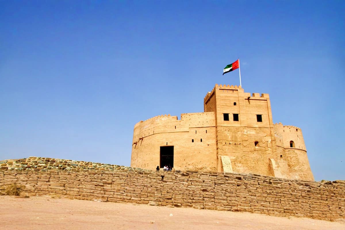 Historic Fujairah Fort with UAE flag flying on top, displaying traditional Arabian architecture against clear blue sky and de