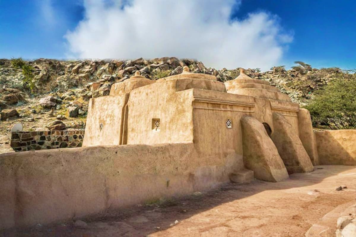 Ancient stone fortification with domed roof and cross-shaped windows set against rocky mountains under blue sky in Fujairah d
