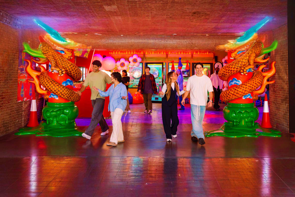 Visitors walking through colorful neon-lit corridor with giant golden dragon statues and vibrant pink and orange decorations 