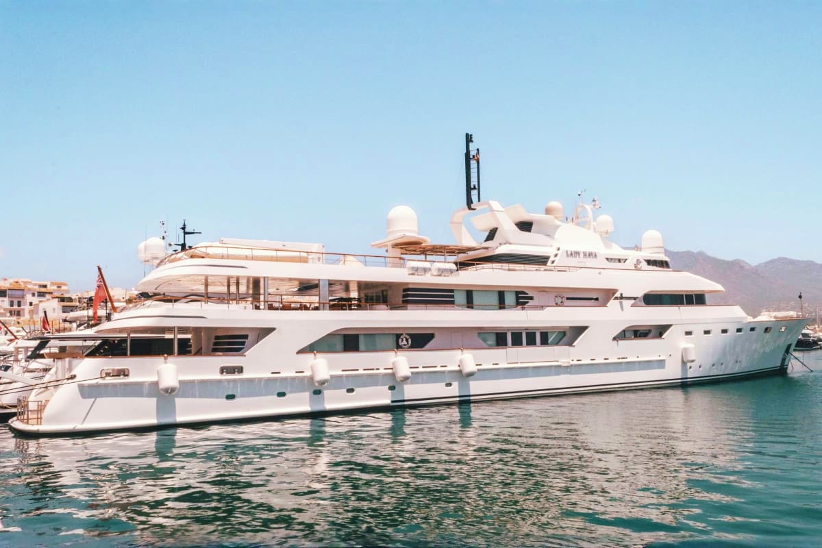 Large white luxury yacht named Lady Maya moored in turquoise Mediterranean harbor with mountains in background