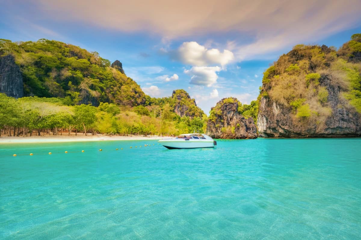 Speedboat anchored in turquoise water near limestone cliffs with beach and mangrove trees at James Bond Island, Thailand