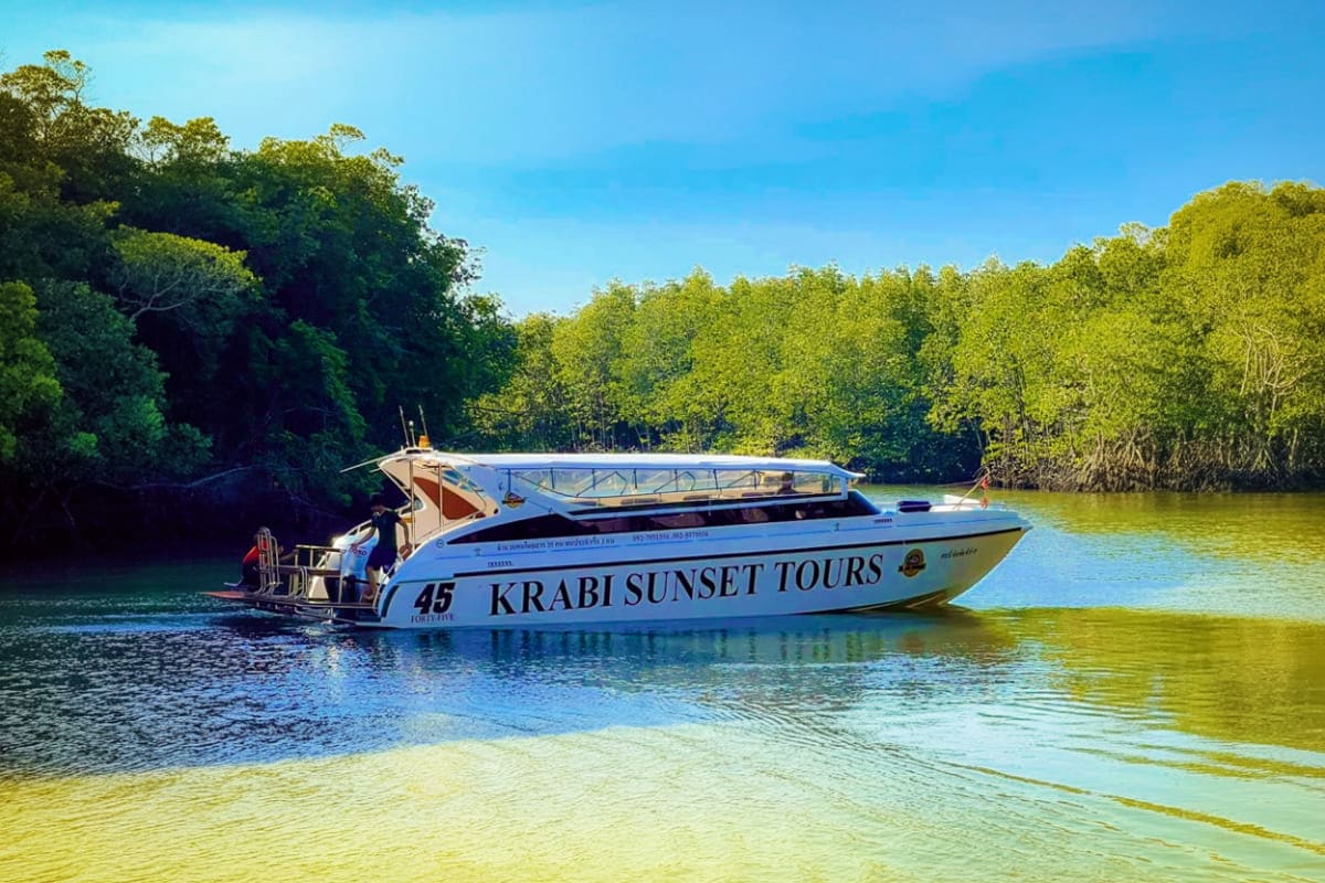 Krabi Sunset Tours speedboat anchored in shallow turquoise water with mangrove forest backdrop in Thailand