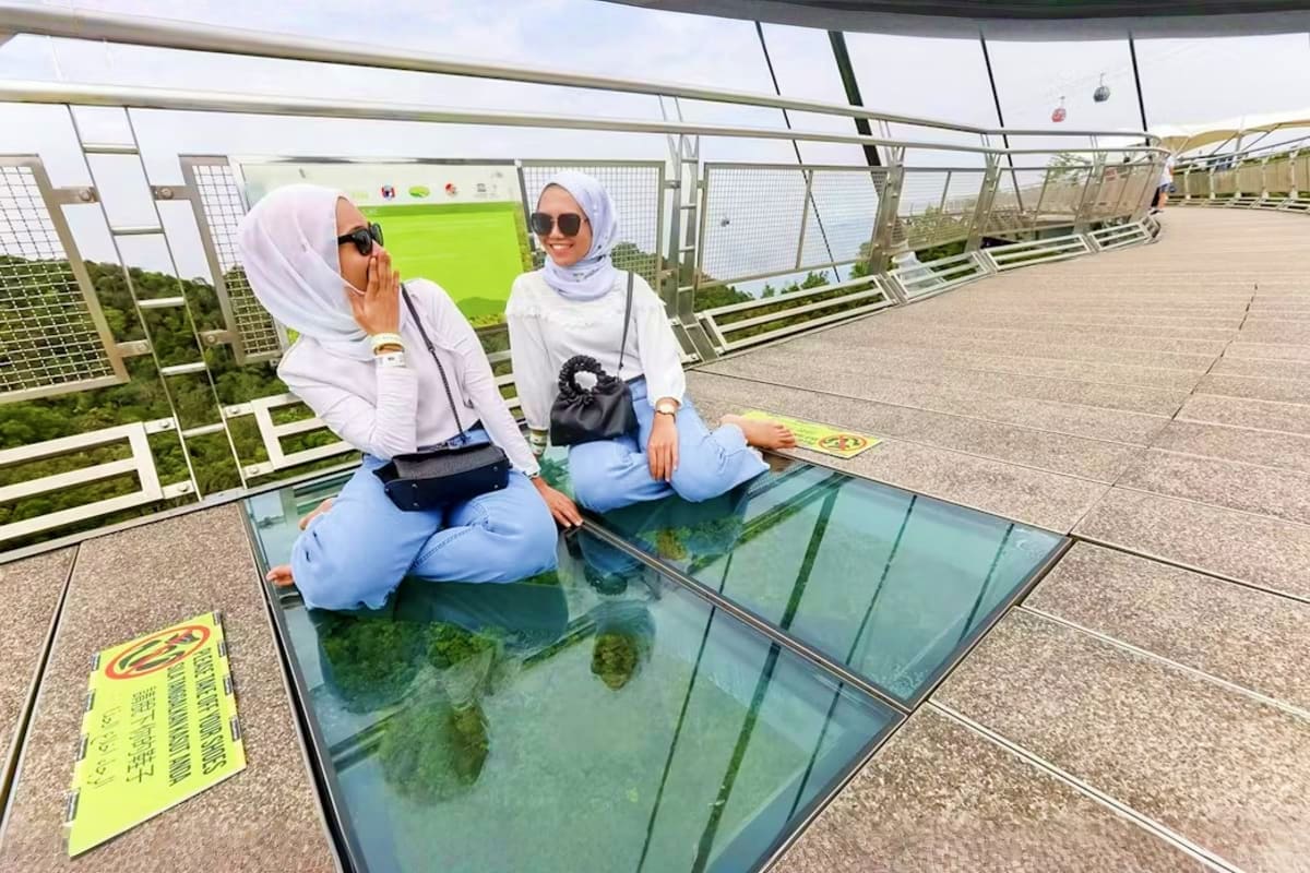 Langkawi Skybridge with Cable Car Ride Two women crouching on glass floor at Langkawi Skybridge viewing gardens below through transparent walkway