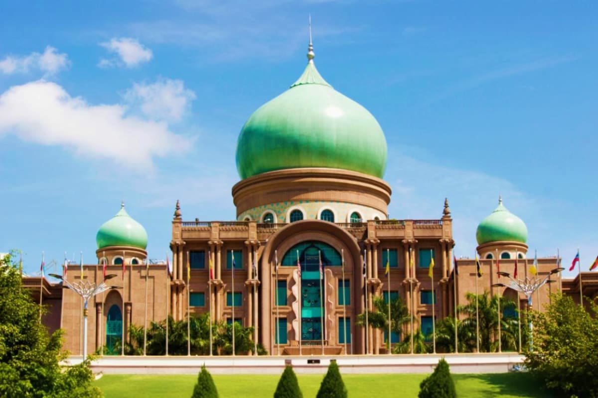 Grand mosque with green domes and brown stone architecture under blue sky, featuring Islamic religious building with manicure