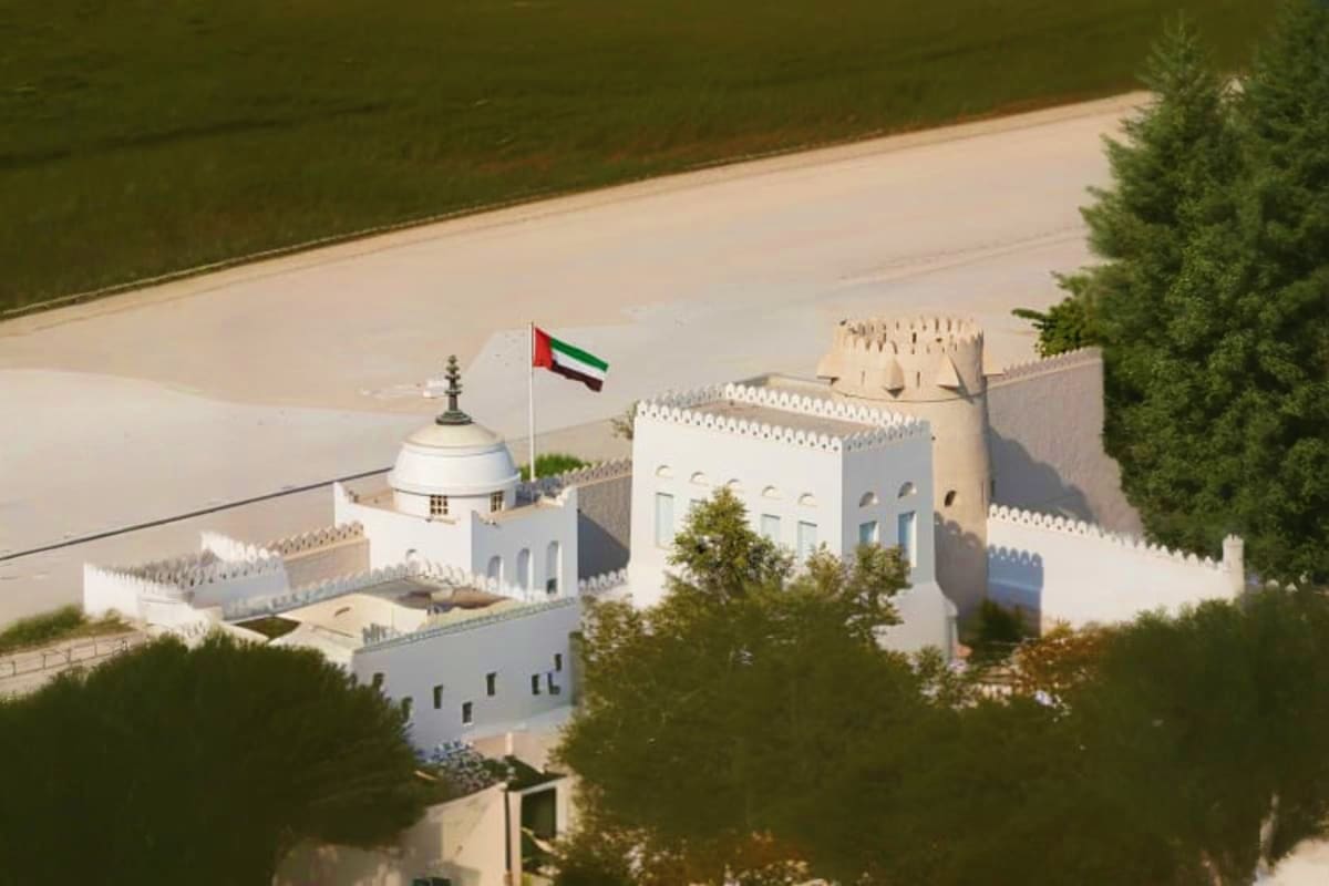 Aerial view of Qasr Al Hosn fort in Abu Dhabi with white walls, UAE flag, and surrounding greenery near waterfront