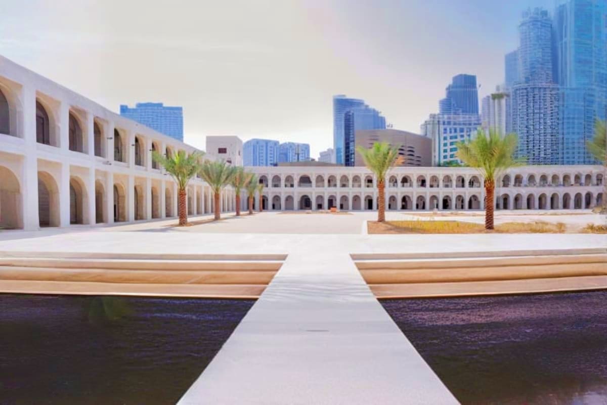 Qasr Al Hosn palace courtyard with symmetrical white arches, palm trees, reflecting pool, and modern Dubai skyline in backgro