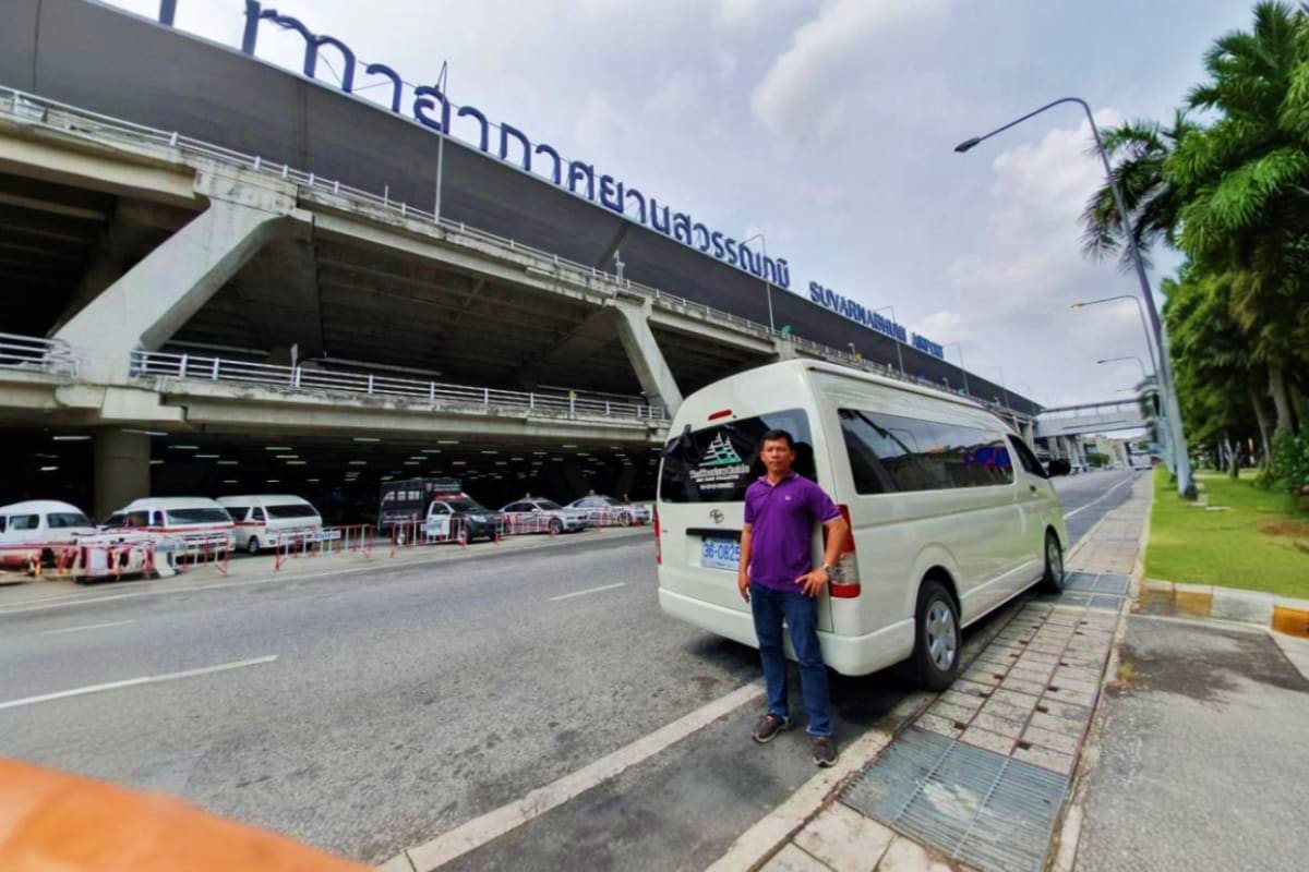 Samui Hotel to Na Thorn Pier White minivan with driver standing beside it at Suvarnabhumi Airport terminal, Thailand airport transfer service
