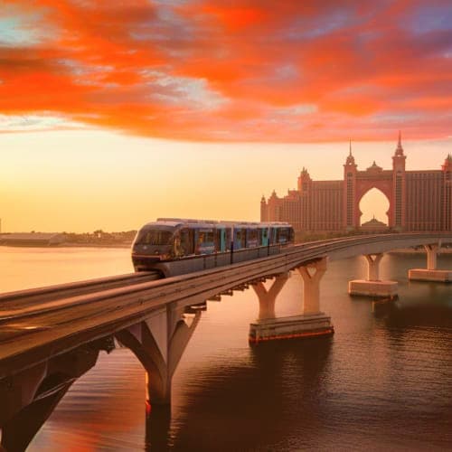 The Palm Monorail Monorail train traveling on elevated track over water at sunset with Atlantis The Palm resort in background, Dubai