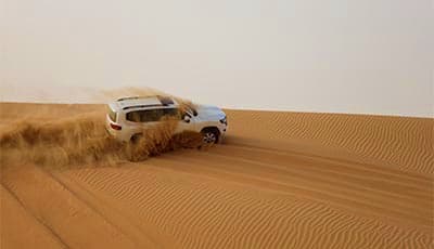 White SUV driving across sand dunes in desert during Abu Dhabi safari