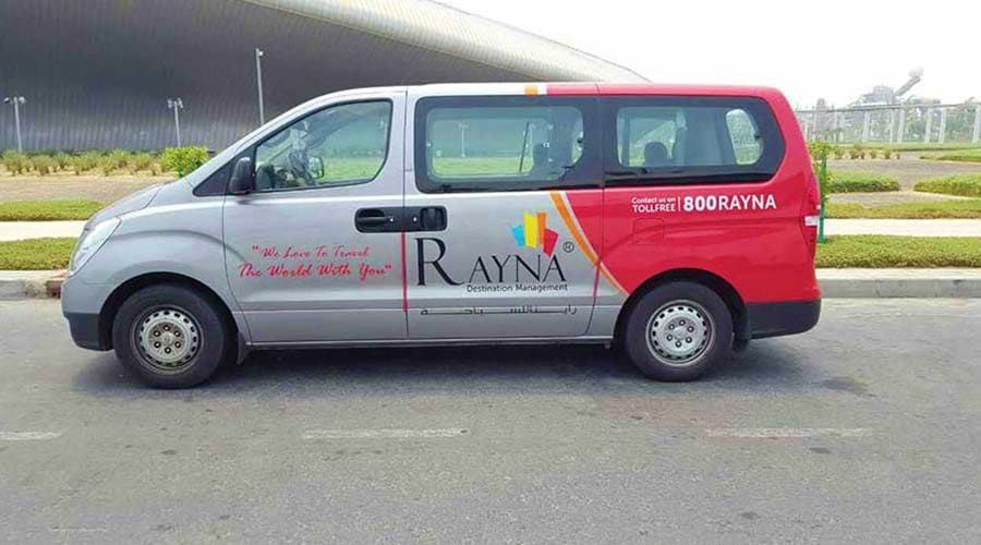 Rayna Destination Management tour van parked in lot, white and red minibus with company branding and 800rayna phone number
