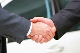 Two businesspeople in dark suits shaking hands in a firm handshake gesture outdoors