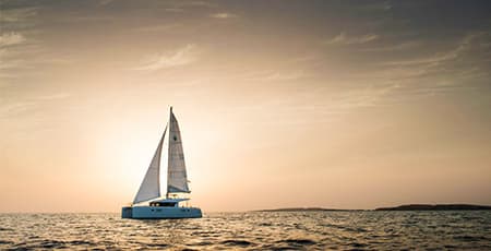 Sailboat with white sails navigating calm waters during golden hour sunset, typical of Damaniyat Island boat tours