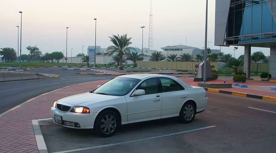 Abu Dhabi to Dubai Intercity transfers White sedan parked on red brick plaza with palm trees and modern buildings in background at UAE transportation hub