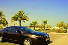 Abu Dhabi to Dubai Intercity transfers Black sedan car parked on desert road lined with palm trees under clear blue sky