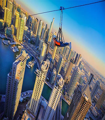 Person on XLine zipline suspended above Dubai Marina with skyscrapers and waterfront visible below on clear day