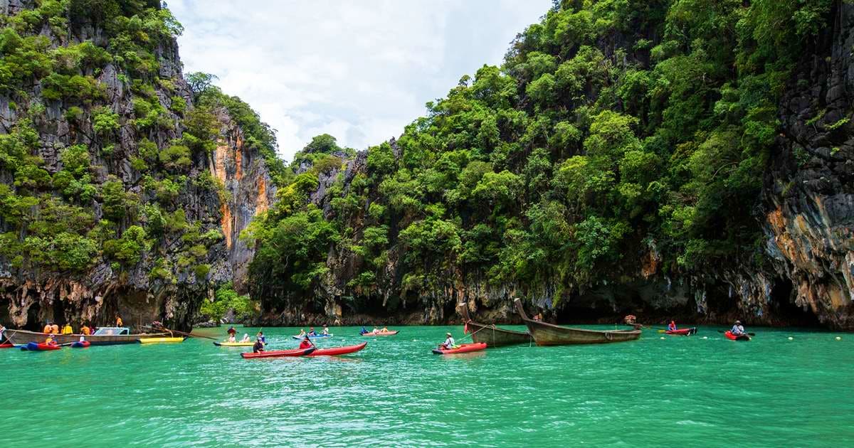 Tourists in colorful kayaks and long tail boats on turquoise water beneath dramatic limestone cliffs in Phang Nga Bay, Thaila