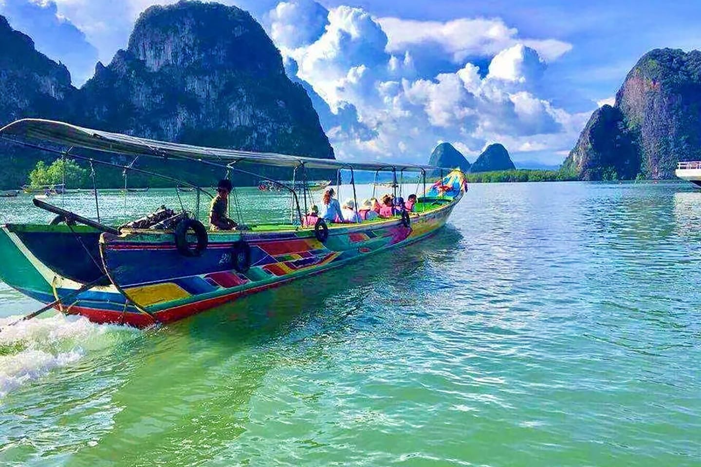Colorful long tail boat with tourists near limestone cliffs in emerald waters, James Bond Island Thailand