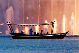 Silhouette of passengers in traditional wooden boat on water with illuminated Dubai Fountain jets in background at night
