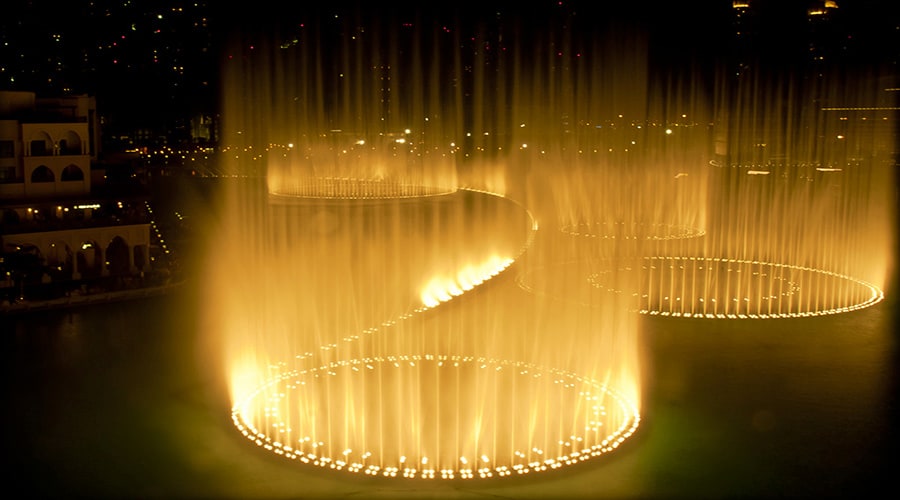 Dubai Fountain Lake Ride from Abu Dhabi Illuminated Dubai Fountain with golden water jets shooting upward at night, creating elegant curved patterns of light and wat