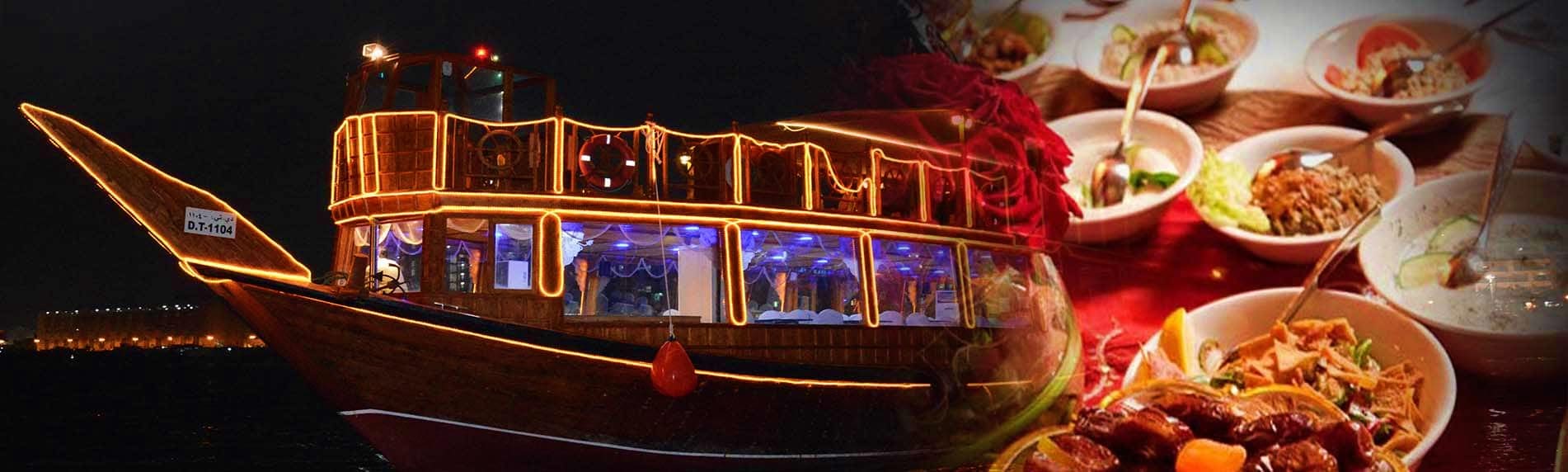Illuminated traditional wooden dhow boat on Dubai Creek at night with Iftar dinner dishes displayed on the right side