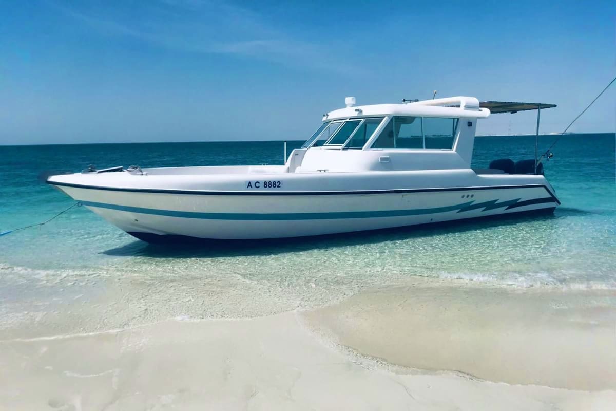 Island Hopping White and teal motorboat AC 8882 anchored in shallow turquoise water near sandy beach under clear blue sky
