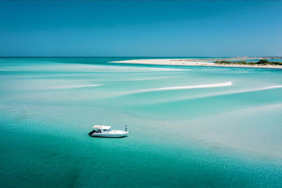 Island Hopping Small white fishing boat anchored in shallow turquoise waters off a pristine sandy beach with clear blue sky