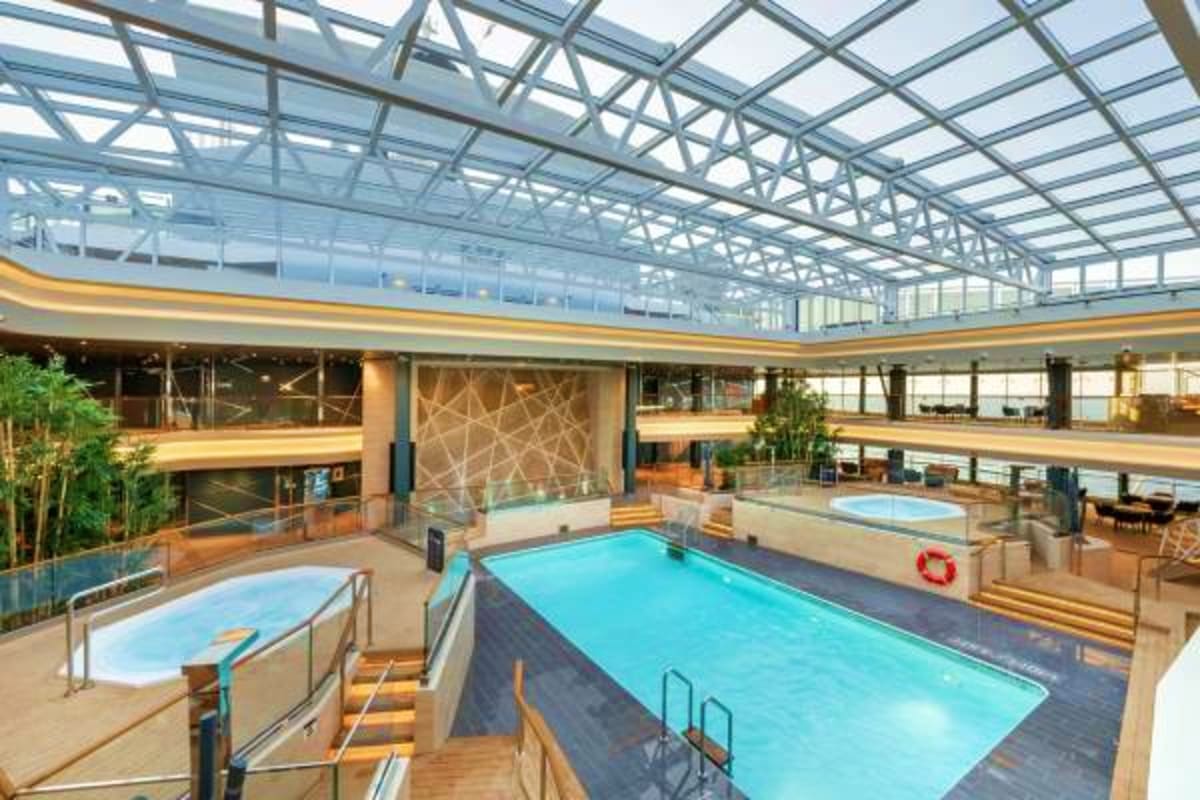 Modern indoor aquatic center with multiple swimming pools, glass roof panels, multi-level galleries, and contemporary lightin