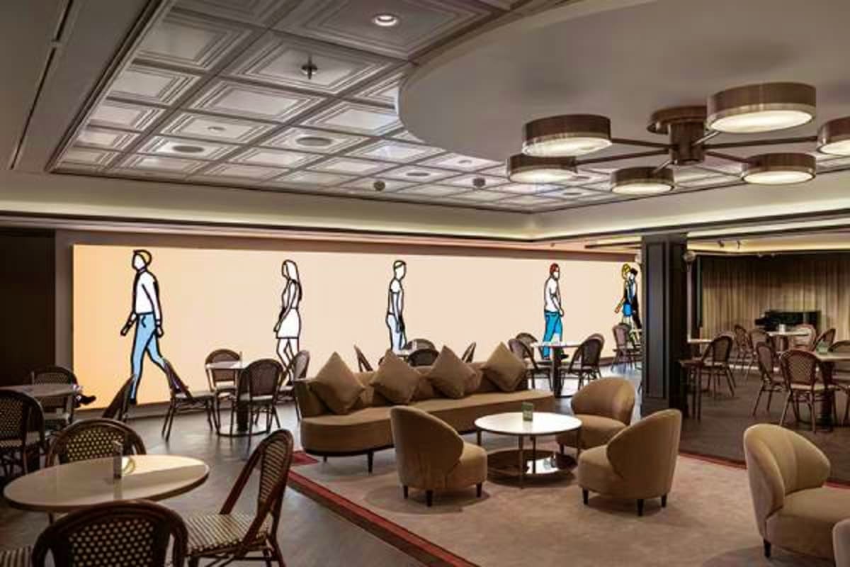 Modern cruise ship lounge with fashion illustration wall art, beige curved seating, round tables, and contemporary ceiling li