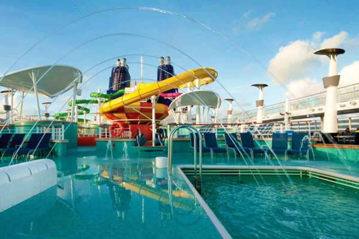 Cruise ship water park with yellow slide, swimming pools, and passengers on sunny deck overlooking ocean