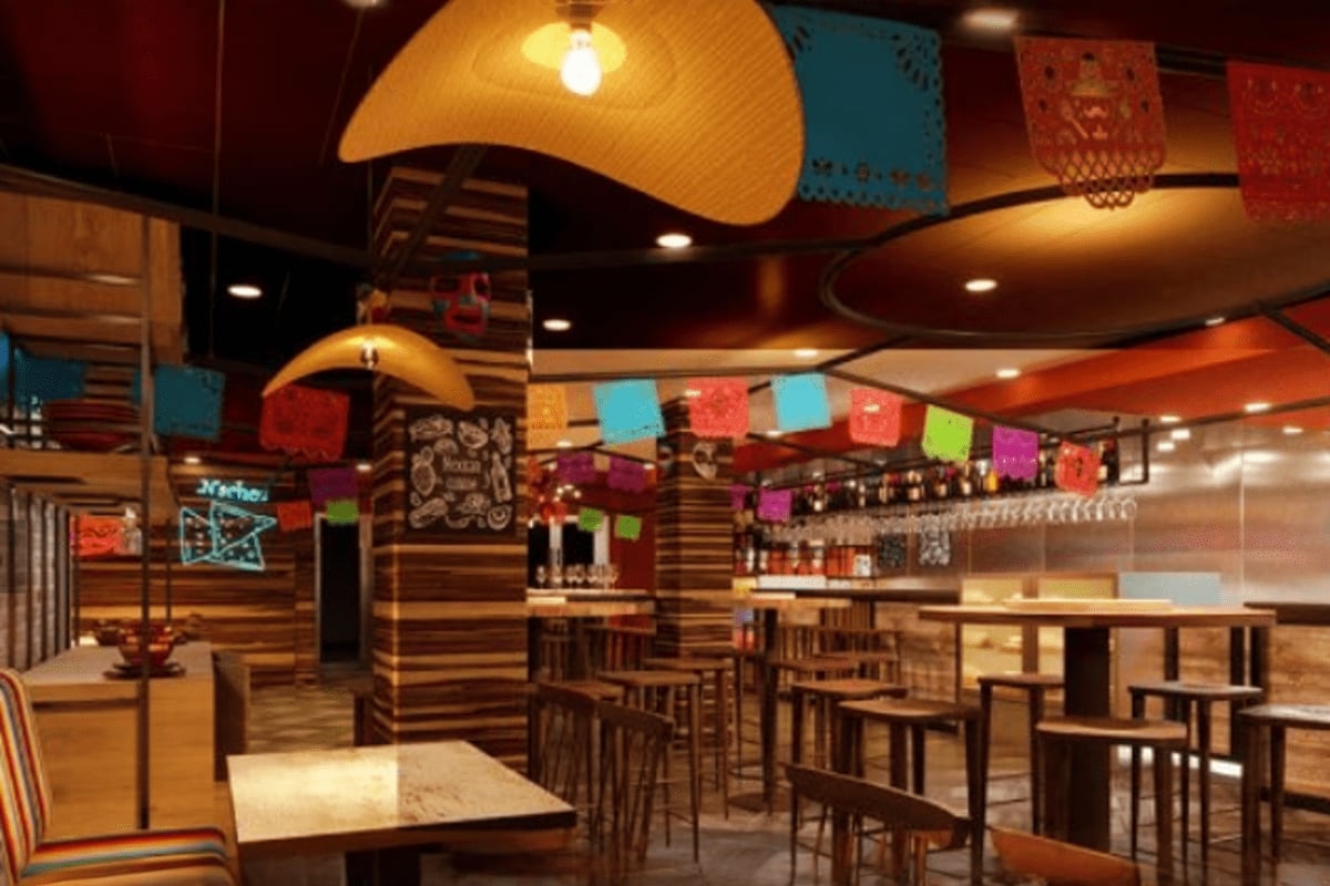 Mexican-themed restaurant interior with colorful papel picado decorations, large sombrero pendant lights, wooden tables and b