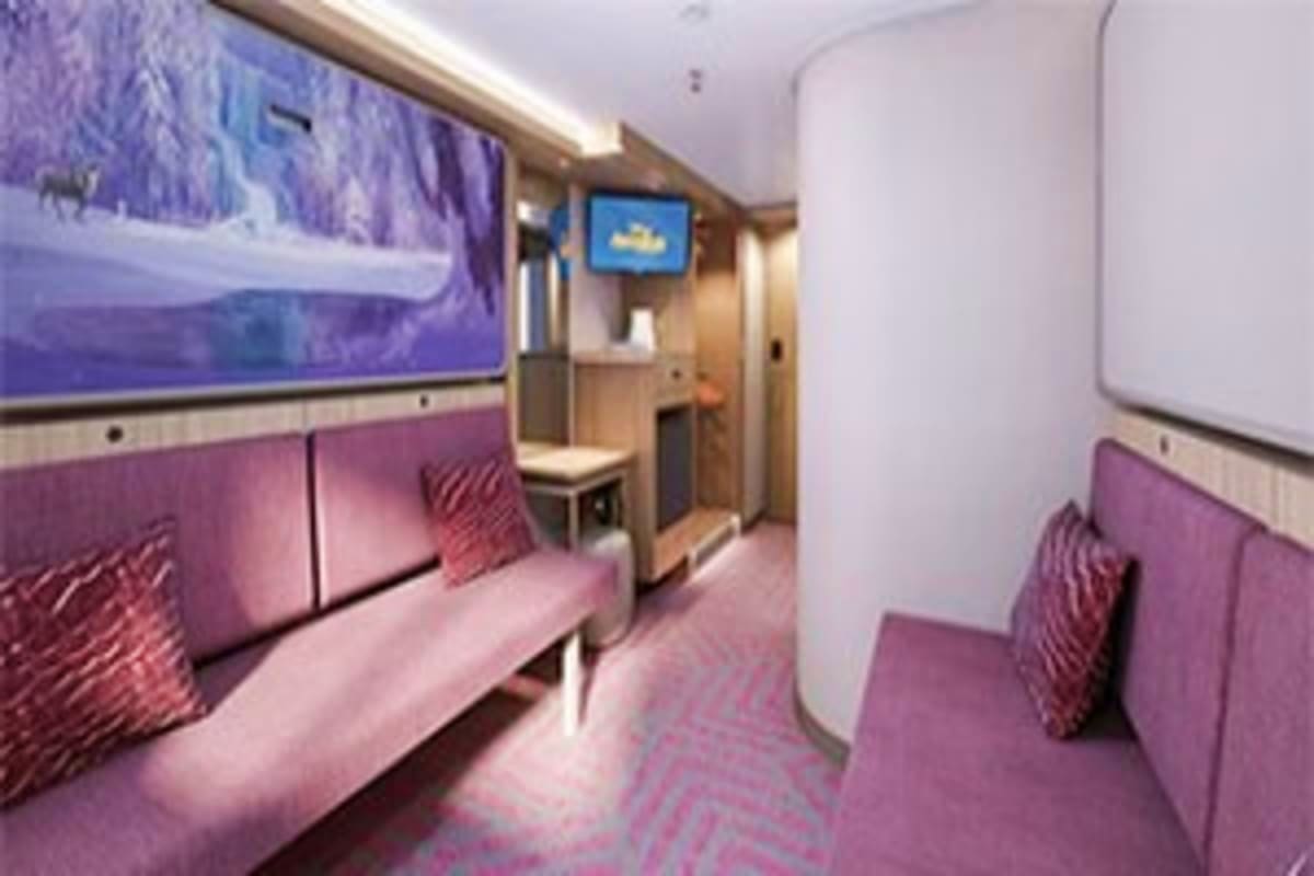 Modern cruise ship interior corridor with purple and pink seating, overhead screens, and cabin doors along the hallway