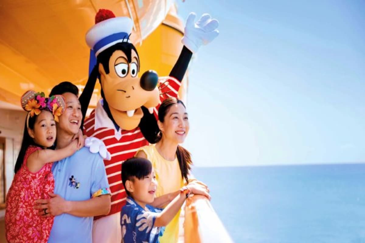 Family with children meeting Goofy character in sailor outfit on Disney cruise ship deck with ocean background