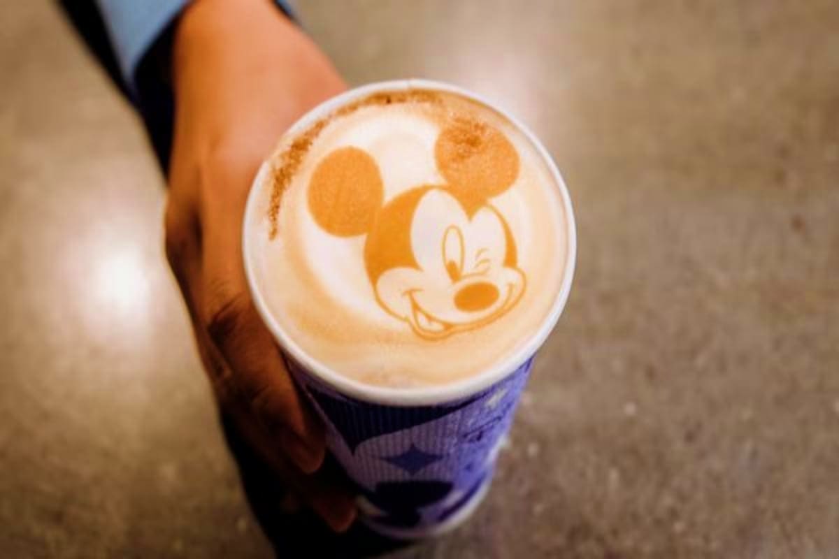 Person holding a coffee cup with Mickey Mouse latte art design