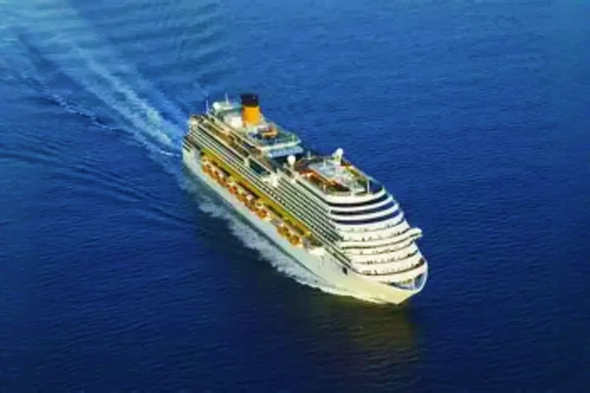 Large white cruise ship with yellow smokestack sailing on deep blue ocean water, aerial view