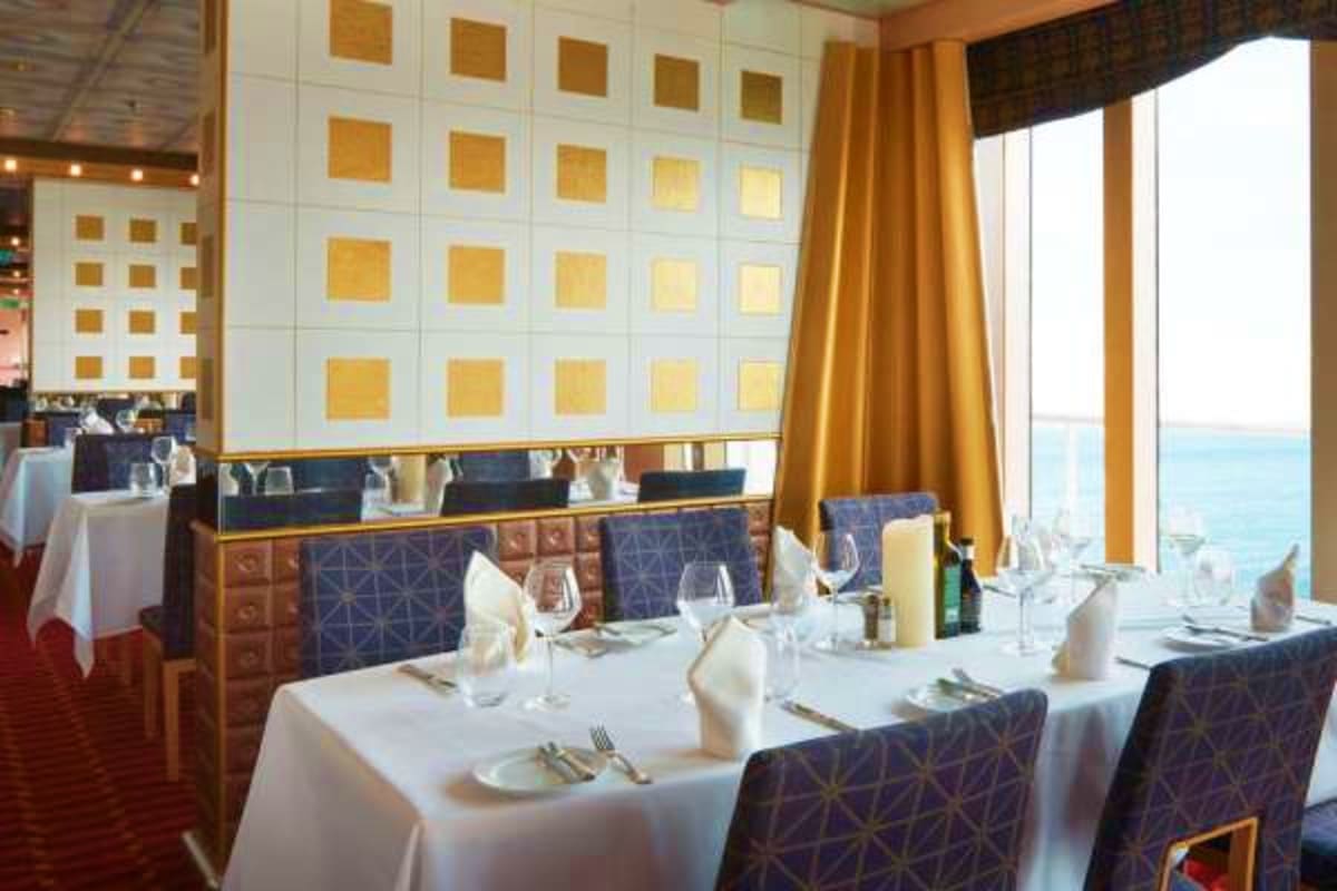 Upscale dining room on cruise ship with white tablecloths, ocean view windows, and gold accents on wall panels