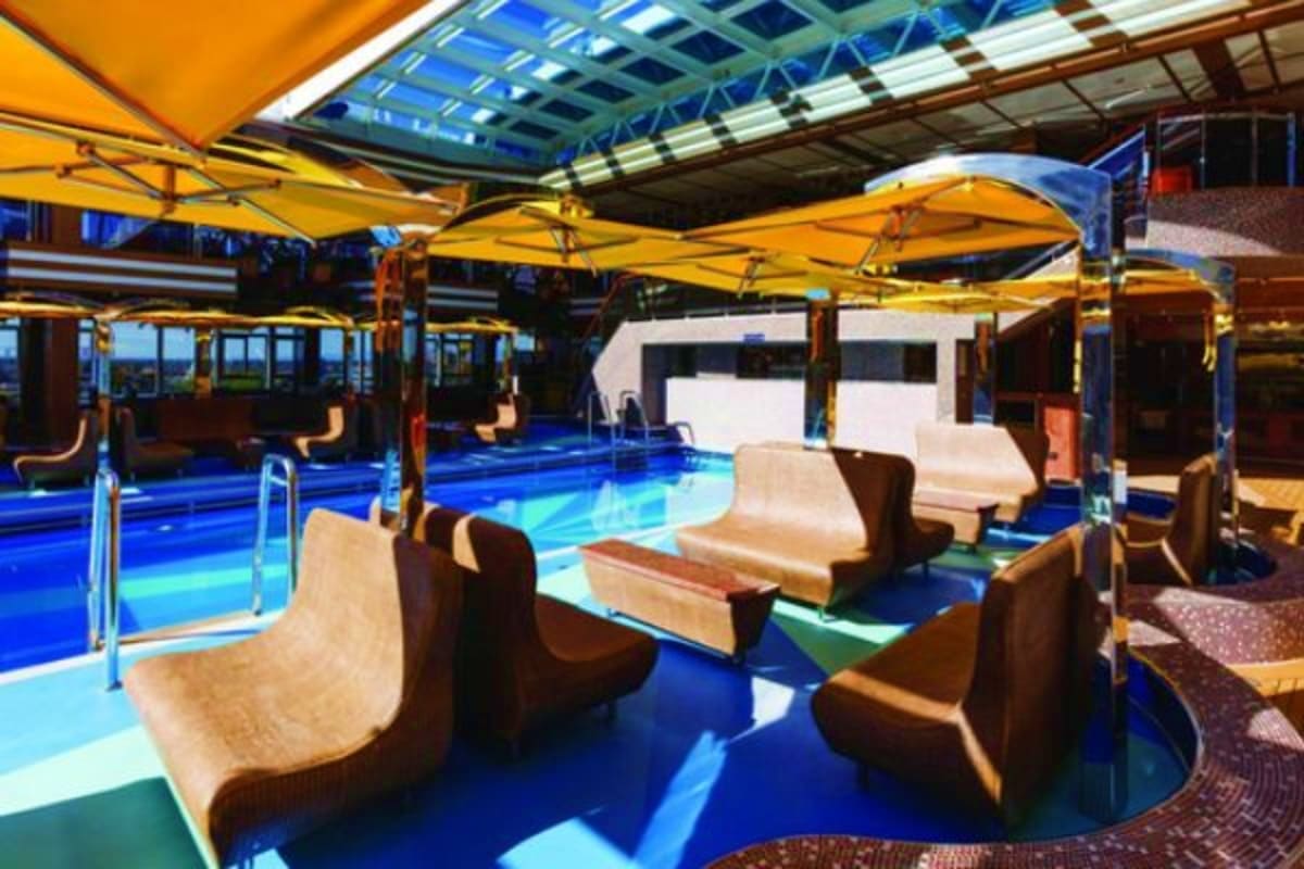 Indoor pool deck with yellow umbrellas, lounge chairs, and glass ceiling on Costa Diadema cruise ship