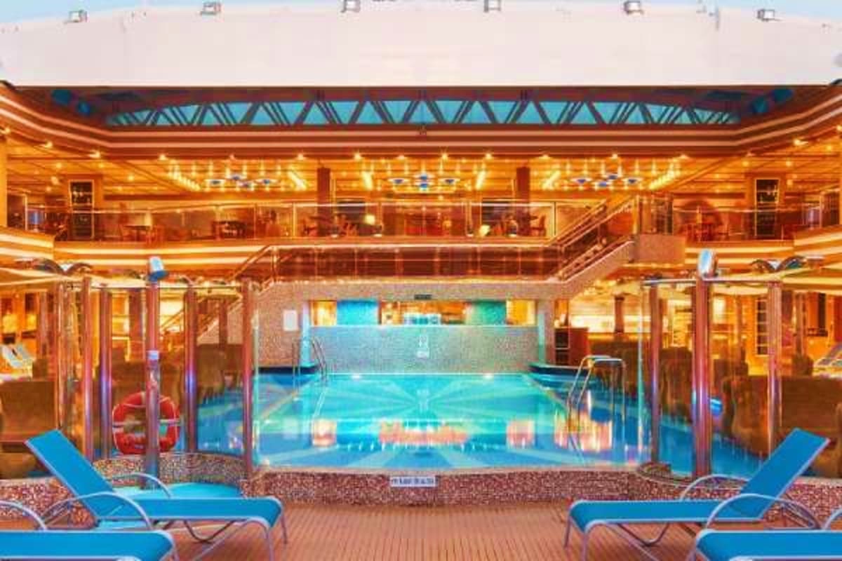 Indoor swimming pool on Costa Diadema cruise ship with blue loungers and multi-level wooden deck surrounding illuminated pool