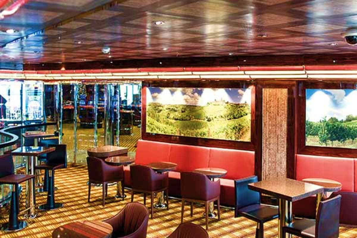 Modern cruise ship lounge with red seating booths, scenic landscape displays on screens, wooden ceiling and polished flooring