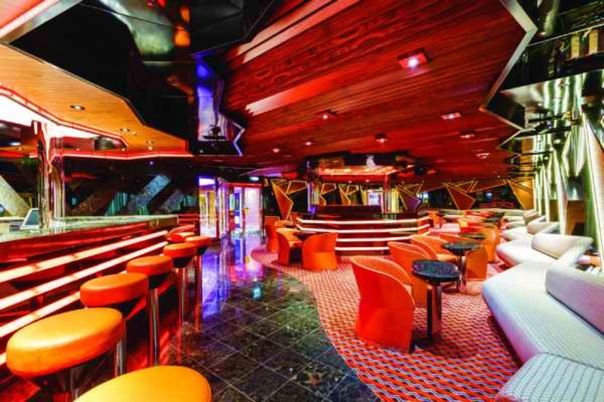 Modern nightclub interior with red ceiling, orange bar seating, white lounge chairs, and neon lighting on cruise ship Diadema