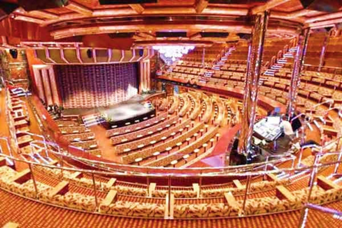 Interior view of Costa Favolosa theater showing curved balcony levels, rows of seats, stage with curtains, and ornate gold an