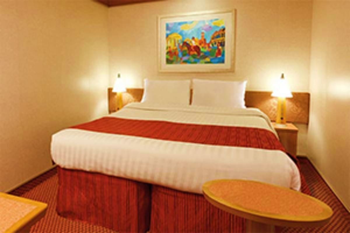 Modern hotel bedroom with double bed, red runner and skirt, wooden nightstands with lamps, and colorful artwork above headboa