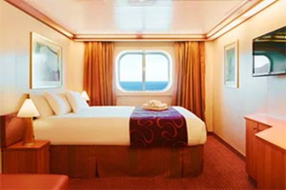 Luxurious cruise ship cabin with queen bed, porthole window overlooking ocean, orange curtains, and warm wood furnishings