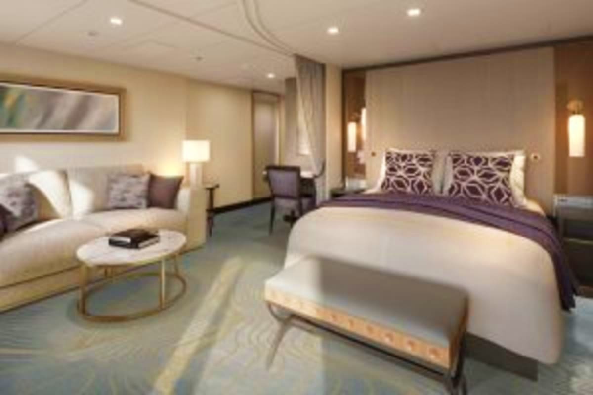 Luxury cruise ship cabin with king bed, seating area, and modern neutral décor featuring beige walls and contemporary furnish