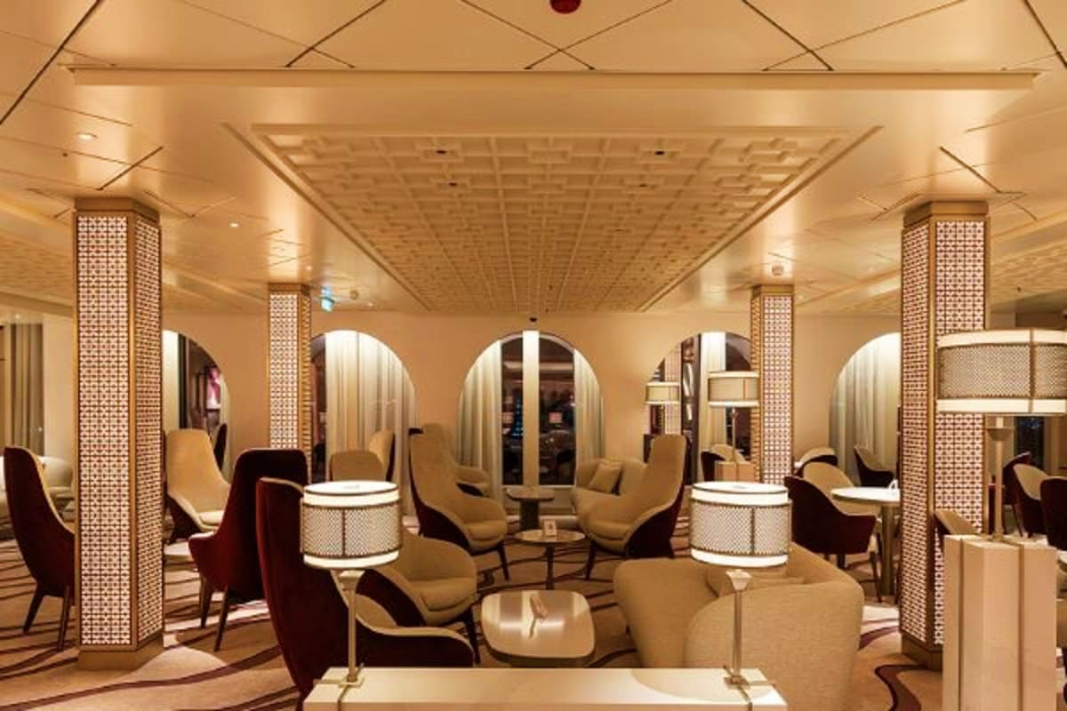 Modern cruise ship spa interior with comfortable seating, arched mirrors, decorative lattice pillars, and warm ambient lighti