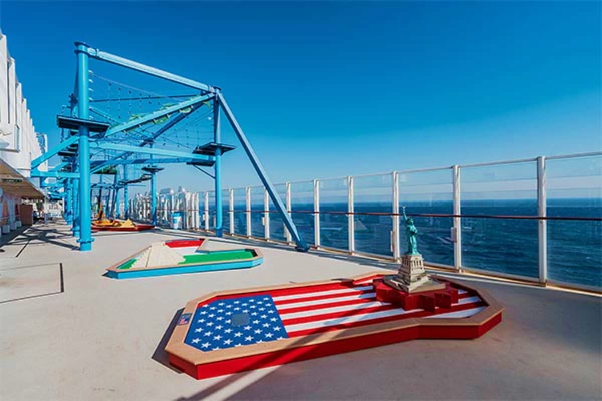 Cruise ship deck with cornhole games and blue recreational equipment overlooking the ocean under clear sky