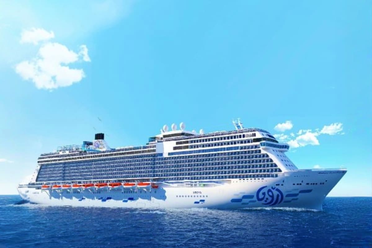 Large modern cruise ship with white hull and blue accents sailing on clear blue ocean under bright sunny sky