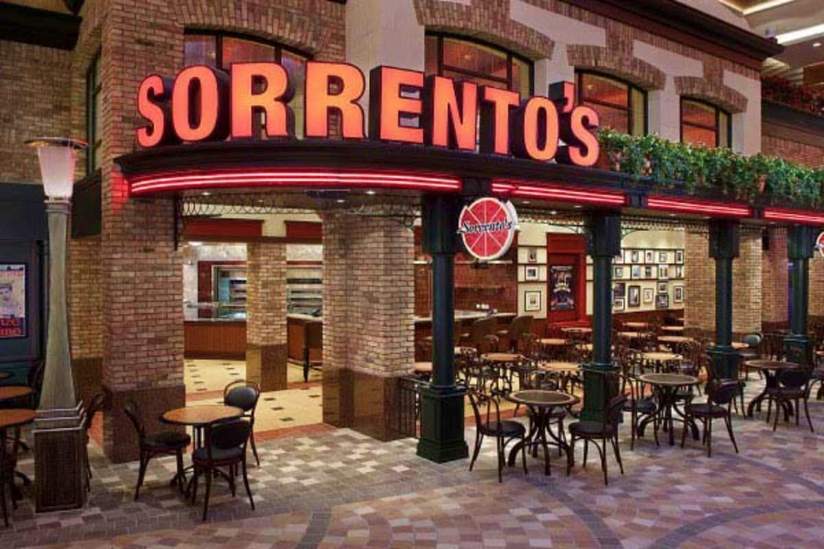 Sorrento's Italian restaurant storefront with red neon sign, brick facade, and outdoor seating area with tables and chairs