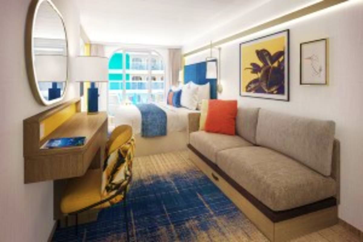 Legend of the Seas Barcelona Roundtrip Cruise Modern cruise ship stateroom with gray sofa, yellow desk, round mirror, blue and yellow artwork, and ocean view window