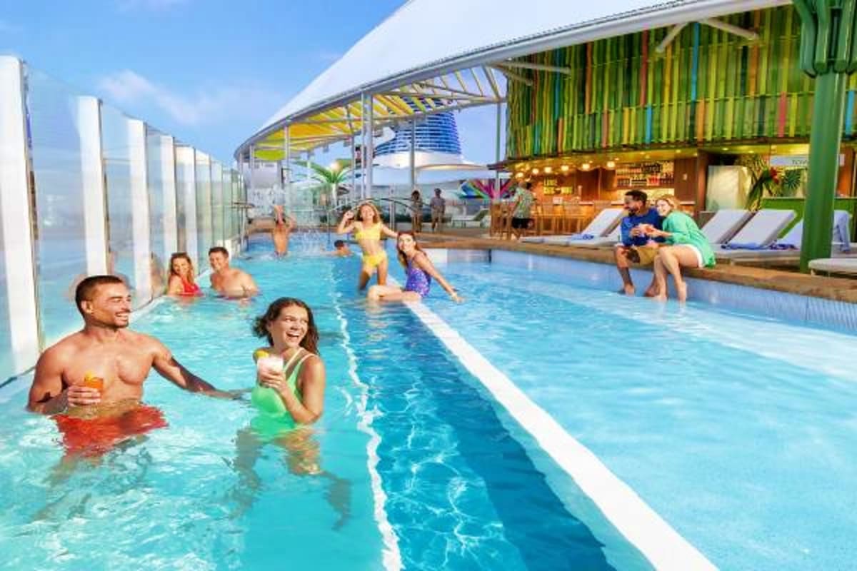 Legend of the Seas Barcelona Roundtrip Cruise Families enjoying an indoor swimming pool on a cruise ship with ocean views and lounge chairs visible in the background